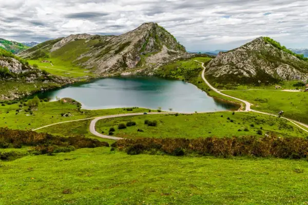 Un lago sereno rodeado de verdes colinas y picos rocosos, un paisaje idílico para ver Picos de Europa.
