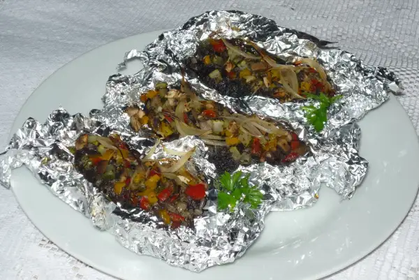 Kaszanka z grilla z cebulą i warzywami, zapieczona w folii aluminiowej, podana na białym talerzu.