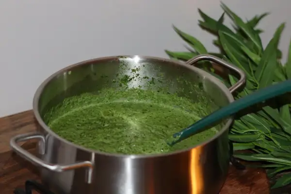 En kastrull med grön spenatsoppa, redo för ett enkelt spenatsoppa recept. Gröna blad syns i bakgrunden.