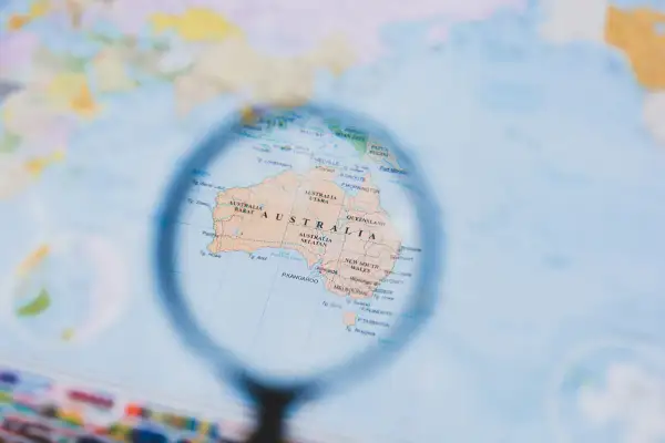 Mapa świata z lupą powiększającą Australię. Planowanie, kiedy są wakacje w Australii, to świetny pomysł na podróż!