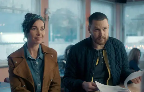 En kvinna med scarf och en man med skägg sitter vid ett bord. Scenen är från en dansk serie på SVT.
