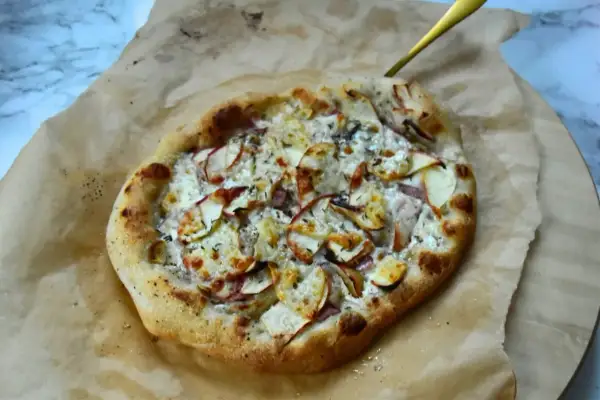 Pyszna pizza bianca z jabłkami i serem, podana na papierze do pieczenia.
