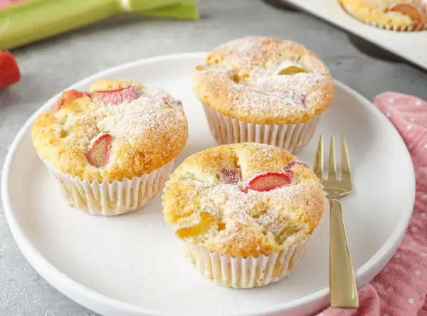 Saftige rhabarber muffins mit joghurt, bestäubt mit Puderzucker, auf einem Teller mit einer goldenen Gabel.