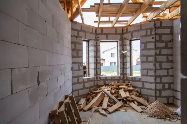 Interno di una casa in costruzione con muri in blocchi di cemento, tetto in legno e cumuli di legname. Forse un caso di abuso edilizio prescrizione.