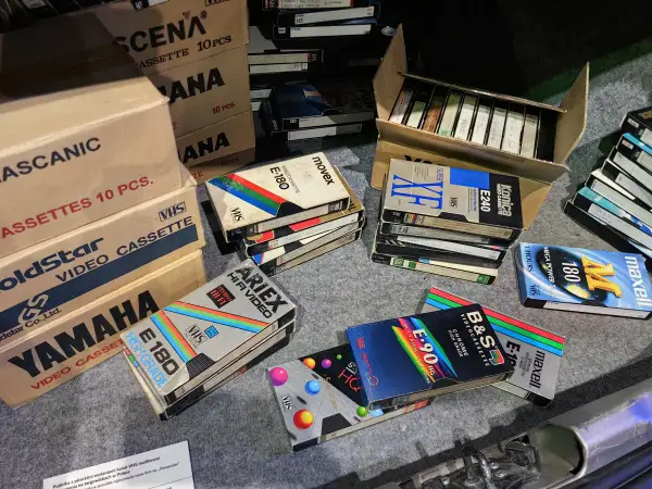 Kolekcja kaset VHS, w tym marki Movix, Konica, Maxell, Ariex, Yamaha. W tle pudełka z kasetami, przypominające o opłacie reprograficznej.