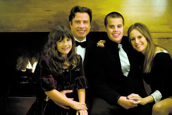 John Travolta med familjen, inklusive sonen Jett, poserar glatt framför en öppen spis.