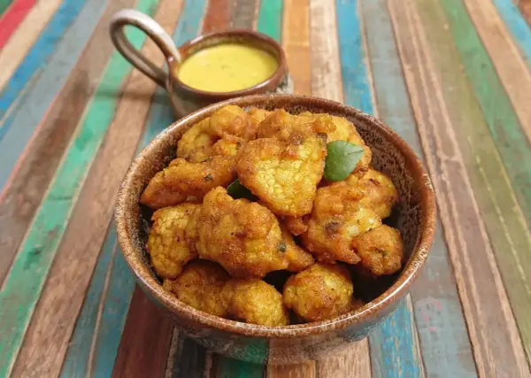 Beignets de choux-fleurs dorés et croustillants, servis dans un bol en terre cuite avec une sauce jaune crémeuse. Parfaits pour un apéritif savoureux.