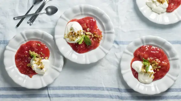 Tre vita skålar med rabarberkompott kardemumma, toppad med grädde och nötter. En härlig dessert.