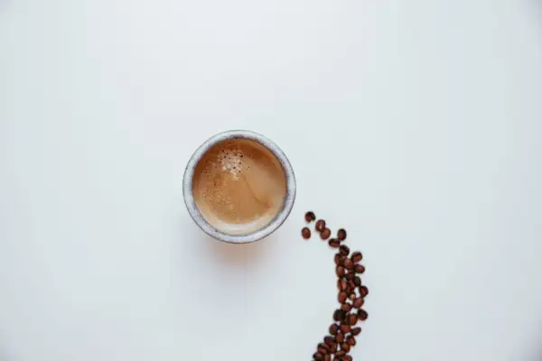 Un caffè pregiato, con la sua crema invitante, accanto a chicchi tostati su sfondo bianco.
