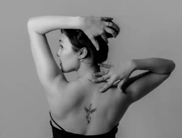 Rückenansicht einer Frau mit einem Phönix-Tattoo, einem der beliebten Tattoos. Ihre Hände sind im Haar und am Nacken.