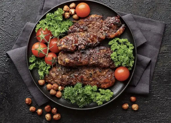 Saftiges Putenschnitzel braten, garniert mit Kirschtomaten, Petersilie und Haselnüssen auf schwarzem Teller.