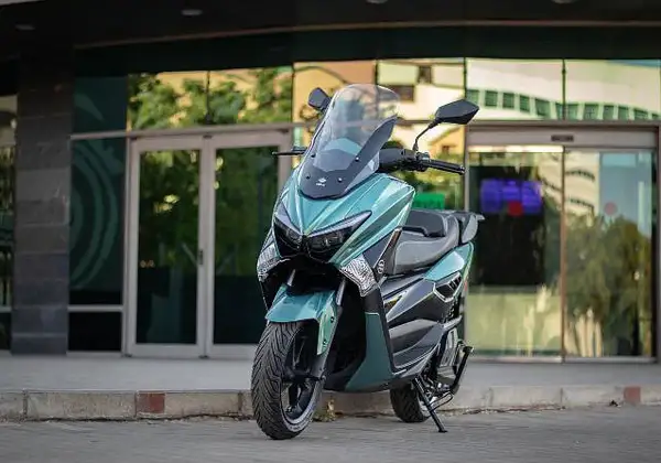 Scooter onex motos color verde menta, con parabrisas alto, estacionada frente a un edificio moderno con puertas de cristal.