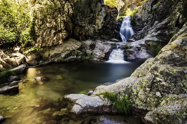 Cascadas escondidas cerca de Madrid, con agua cristalina cayendo entre rocas cubiertas de musgo y vegetación exuberante.