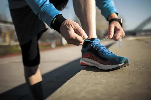 Un coureur attache ses lacets bleus, prêt à laisser une trace de frottement chaussure sur le bitume.