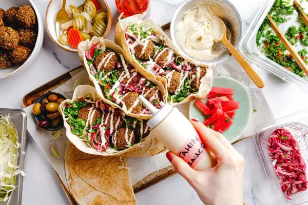 Leckeres Falafel-Rezept: Pita gefüllt mit Falafel, Salat, roten Zwiebeln und Tahini-Sauce. Dazu Hummus, Oliven und eingelegtes Gemüse.