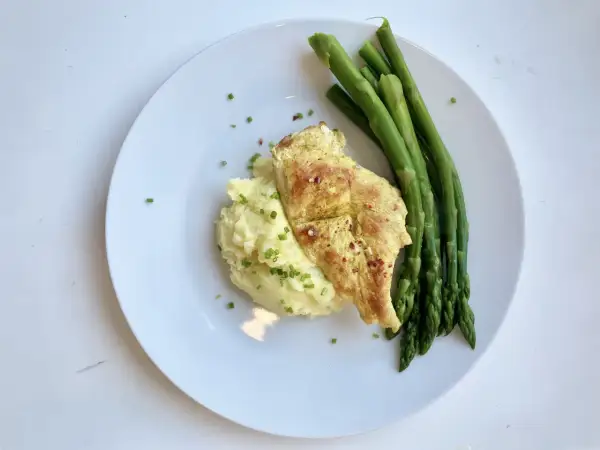 Na talerzu kurczak z puree ziemniaczanym, które jest źródłem węglowodanów, i zielone szparagi.