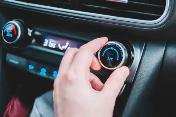 En hand vrider på reglaget för ac i bilen. Temperaturen sjunker snabbt.