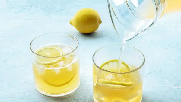 Erfrischendes Wasser mit Zitrone wird morgens in ein Glas mit Eis und Zitronenscheiben gegossen.