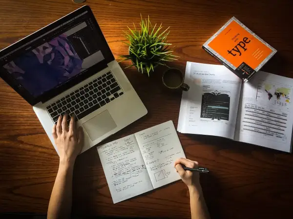 Ręce pracują nad projektem, laptop, notatnik i książka o typografii. To idealne warunki do start up.