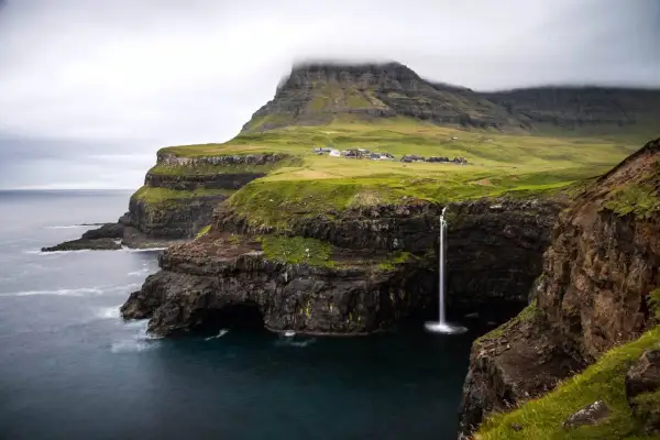 Paysage spectaculaire des îles Féroé : une cascade tombe d'une falaise verdoyante dans l'océan. Idéal pour une randonnée inoubliable.
