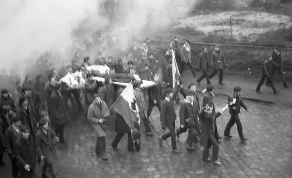 Tłum niesie nosze z ciałem, dym unosi się w powietrzu. Janek Wiśniewski padł, a jego towarzysze idą dalej.
