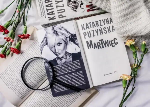 Książki Katarzyny Puzyńskiej, kwiaty i szkło powiększające na białym tle.