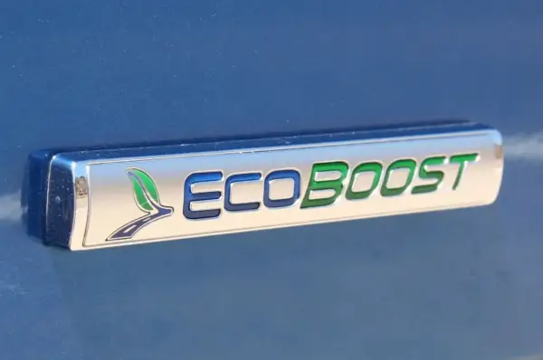 Ford Focus 1.0 EcoBoost kamremsbyte pris. Ett emblem på en blå bil visar "ECOBOOST" med gröna och blå bokstäver.