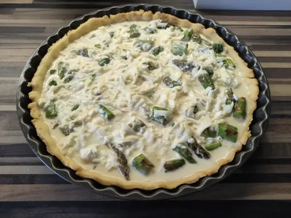 Tarta ze szparagami, gotowa do pieczenia, z kremowym nadzieniem i serem.