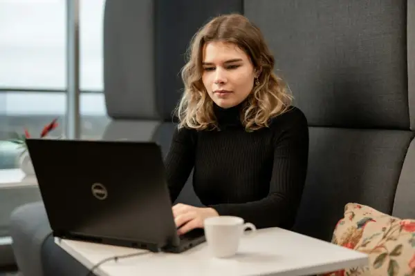 Młoda kobieta z wrodzonymi zdolnościami do pracy przy laptopie, skupiona na zadaniu. Obok filiżanka kawy.