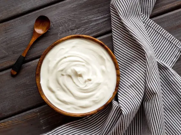 Prosty krem z mascarpone i jogurtu w drewnianej misce, obok drewniana łyżka i pasiasty ręcznik.