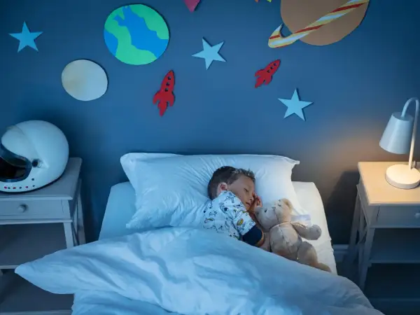 Kleiner Junge schläft im Weltraum-Kinderzimmer. Die kinderzimmer wandgestaltung mit Planeten und Raketen inspiriert Träume von Abenteuern.