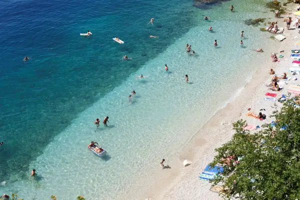 Słoneczne rijeka plaże z turkusową wodą. Ludzie pływają, opalają się i relaksują na kamienistym brzegu.