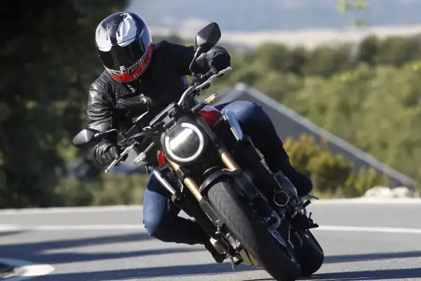 Motociclista con casco Venom en pleno rodaje moto, inclinado en una curva con paisaje verde de fondo.