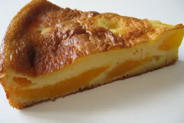 Tranche de clafoutis aux pêches, dorée et moelleuse, avec des morceaux de fruits juteux.