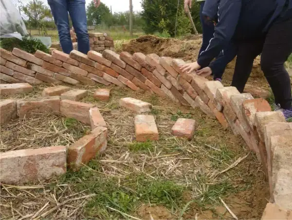 Costruzione di un keyhole garden con mattoni. Mani che posizionano i mattoni per creare la forma circolare.