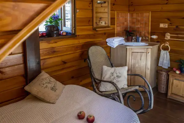 Przytulny pokój w stylu agroturystyka Podlasie. Drewniane ściany, łóżko, fotel bujany i łazienka.