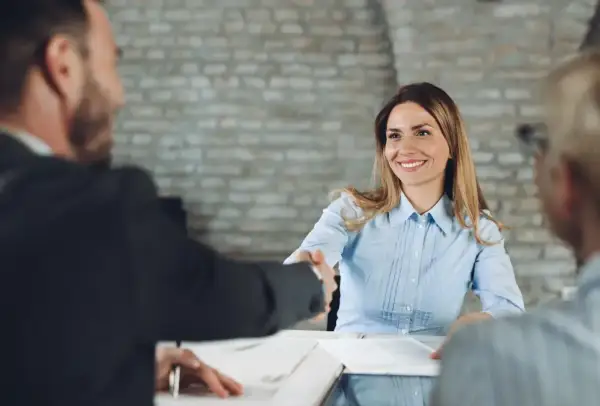 Uśmiechnięta kobieta podaje rękę mężczyźnie. Rozmowa przebiega pomyślnie, a tematy do rozmowy wydają się być interesujące dla obu stron.