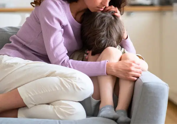 En mamma tröstar sitt barn som kramar sina knän. Barnet verkar oroligt, kanske upplever separationsångest.
