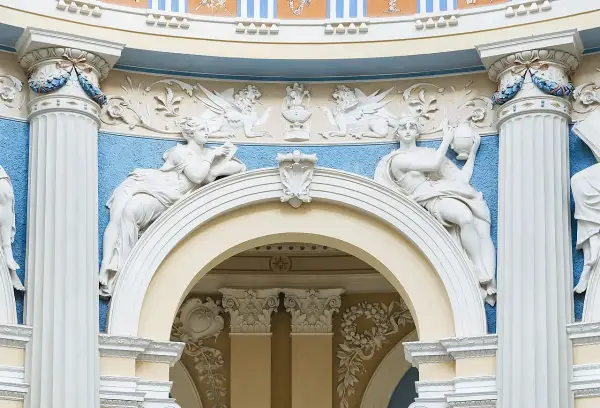 Barokowe stiuki: rzeźby kobiet, gryfy i ornamenty na tle błękitnej ściany.