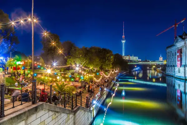 Serata vivace in un club all'aperto a Berlino, con luci colorate, gente che balla e la Torre della Televisione sullo sfondo.