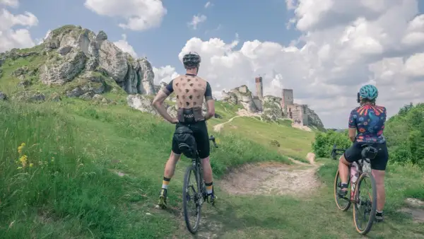 Dwaj rowerzyści podziwiają ruiny zamku na tle skalistego krajobrazu. To idealne miejsce na przejażdżkę rowerowy szlak orlich gniazd.