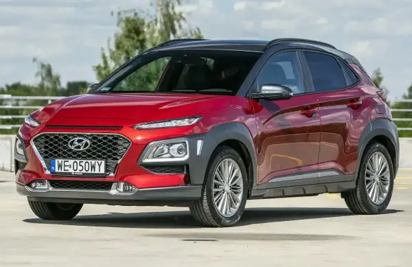 Czerwony, mały SUV dla kobiety, Hyundai Kona, z czarnym dachem, zaparkowany na zewnątrz.