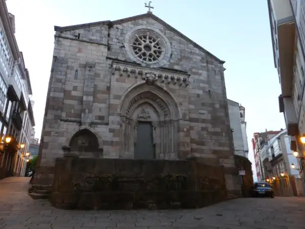 La iglesia de Santiago a Coruña, con su fachada de piedra y rosetón, se alza imponente en una calle adoquinada.