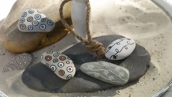 Ideas para pintar piedras de playa: piedras decoradas con círculos concéntricos y líneas onduladas en tonos tierra y blanco.