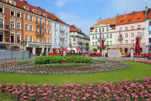 Kolorowy rynek w najstarszym mieście w Polsce, z kwitnącymi rabatami kwiatowymi i kolorowymi kamienicami w tle.