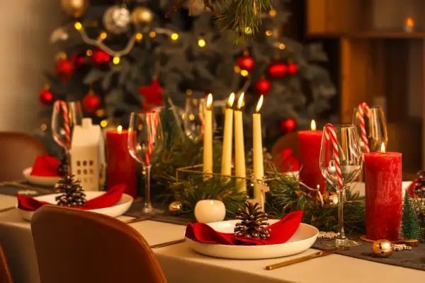 Uroczysta wigilia w restauracji: pięknie nakryty stół z czerwonymi świecami, szyszkami i choinką w tle.