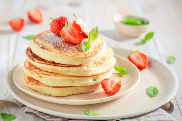 Pancake con yogurt e fragole fresche, spolverati di zucchero a velo e decorati con foglie di menta.