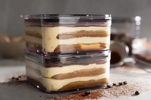 Zwei Schichten sally tiramisu im transparenten Behälter, mit Kakaopulver und Kaffeebohnen bestreut.