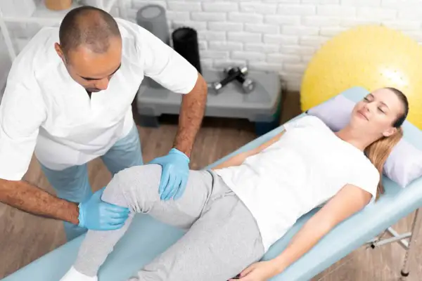 Fizjoterapeuta wykonuje masaż podczas rehabilitacji po operacji kolana. Kobieta leży na kozetce, zrelaksowana.