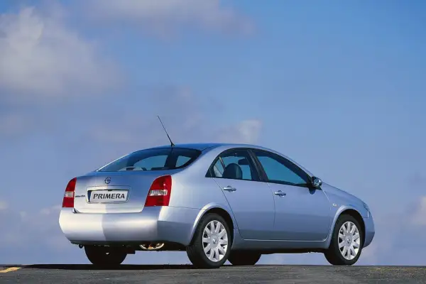 Srebrny Nissan Primera 2002 z widokiem z tyłu, zaparkowany na drodze pod błękitnym niebem.